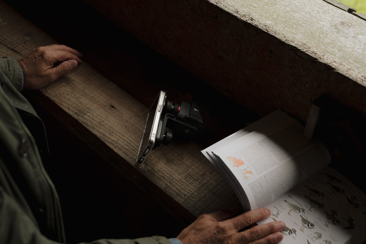 Kite Stabi One mounted on smartphone resting on bird hide ledge next to open bird field guide