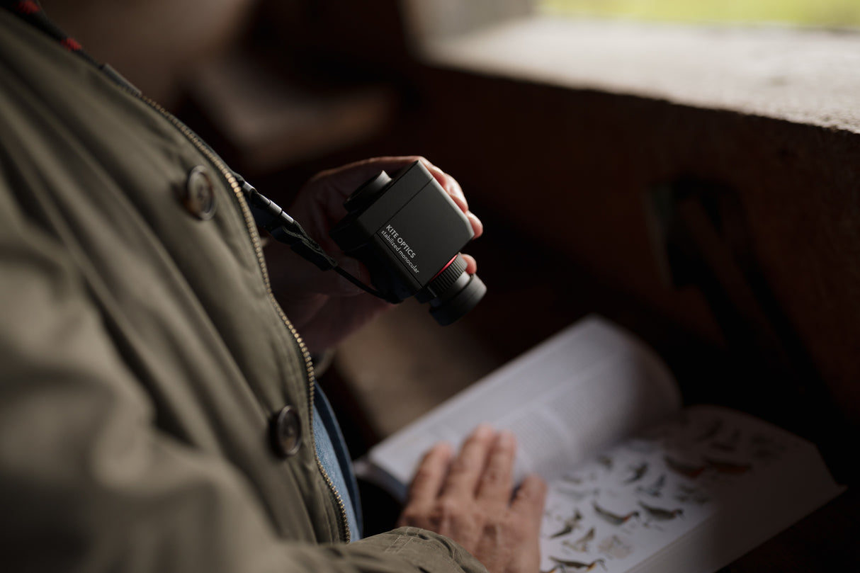 Close-up of Kite Stabi One held in hand next to bird identification field guide in bird hide