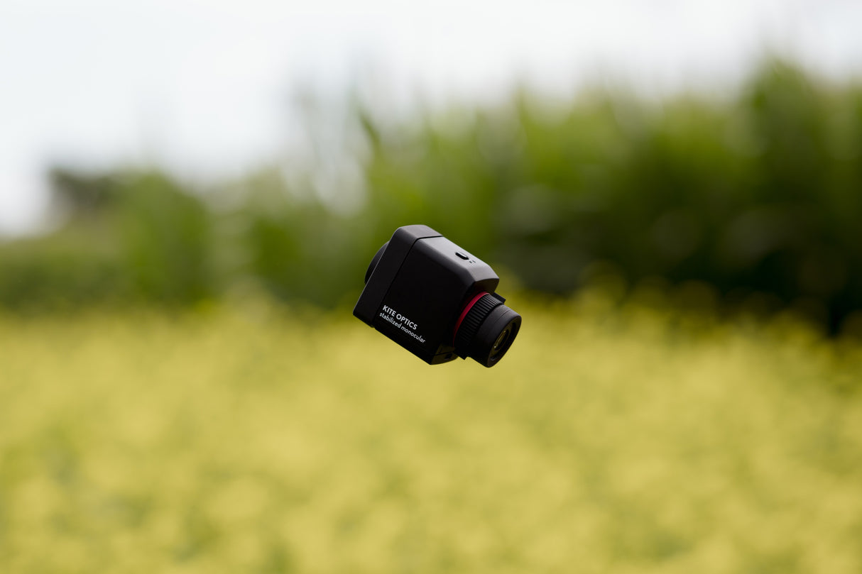 Kite Stabi One suspended in air against green field bokeh, showing Kite Optics branding