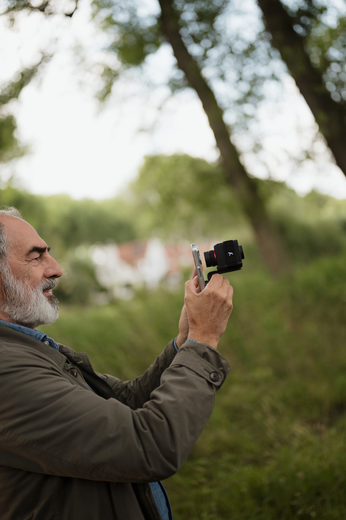 Side profile of man digiscoping with Kite Stabi One on smartphone in rural landscape