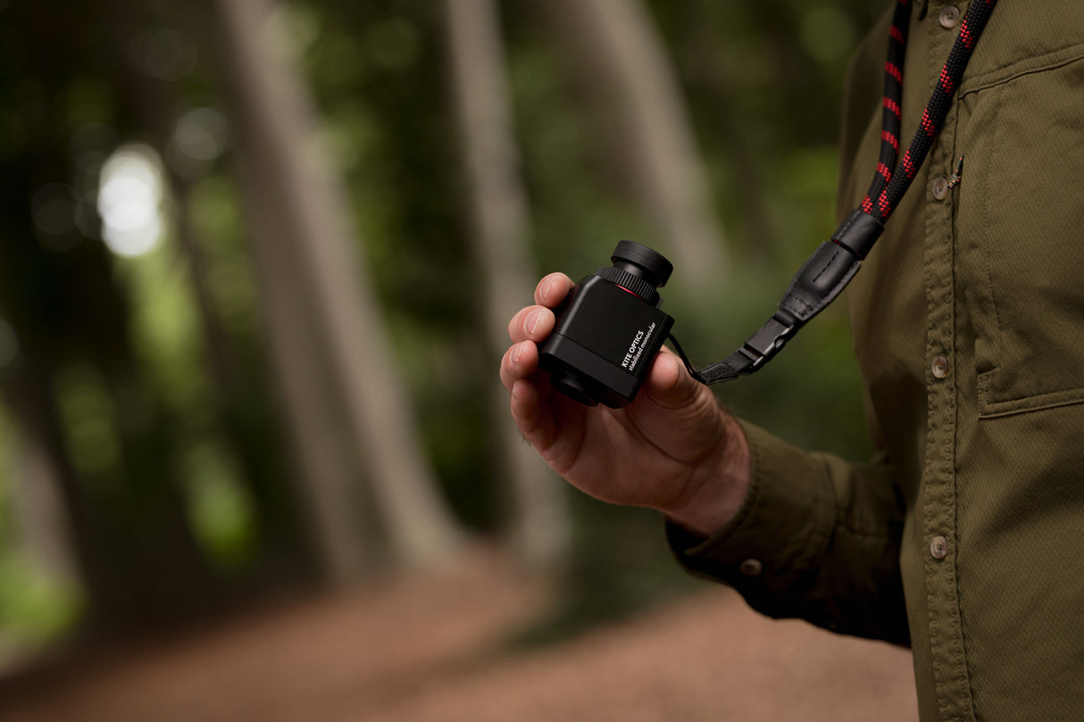 Close-up of Kite Stabi One held in palm showing compact size with forest backdrop and neoprene strap
