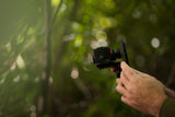 Close-up of hand holding Kite Stabi One with phone mount in forest with bokeh green background