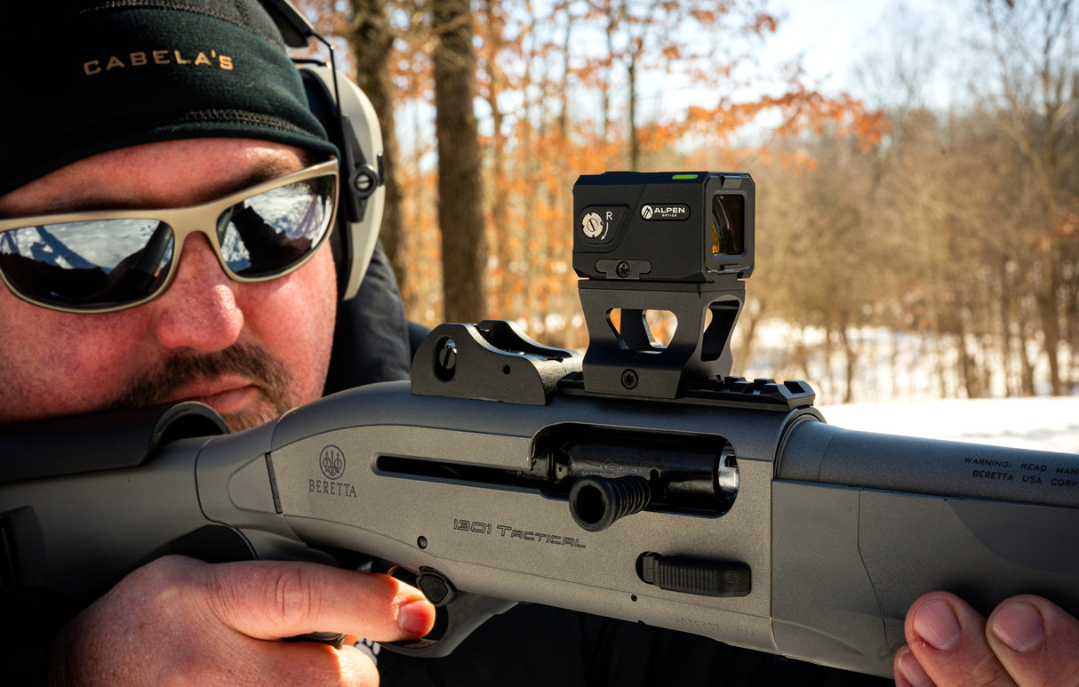 Alpen Argus LT 1x20 enclosed red dot mounted on a pistol slide in an outdoor range setting with the target blurred in the background