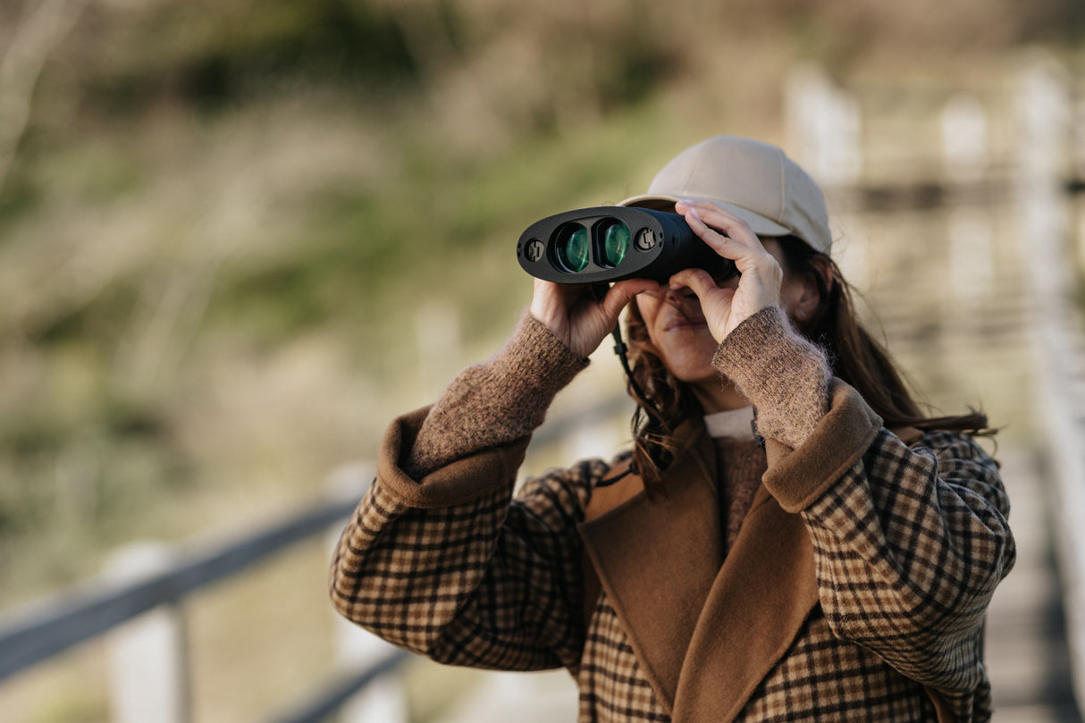 Woman using Kite Optics APC 42 stabilized binoculars for birdwatching outdoors at a coastal nature reserve