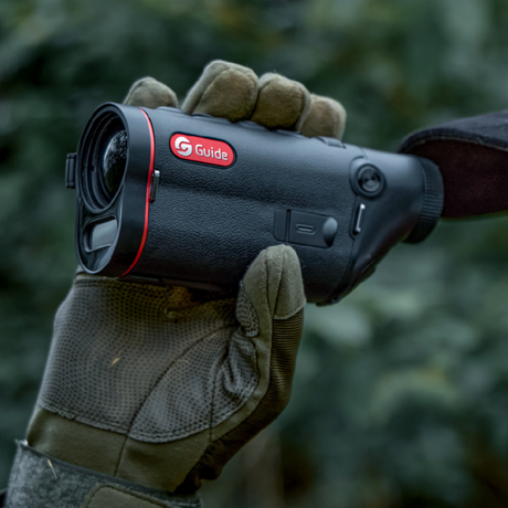 Guide TD 653L thermal monocular held in gloved hand in the field, demonstrating compact one-handed operation