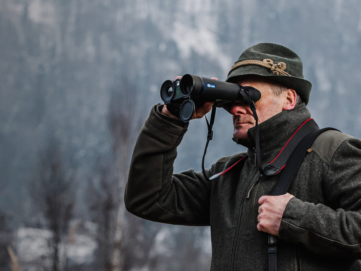 Man using the Guide DN70M 2.0 thermal and 4K digital binocular in a snowy forest